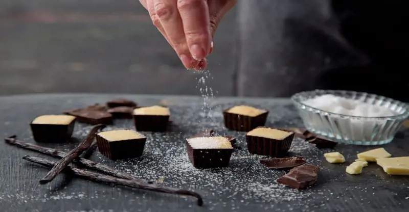 Hand sprinkling icing sugar over chocolate
