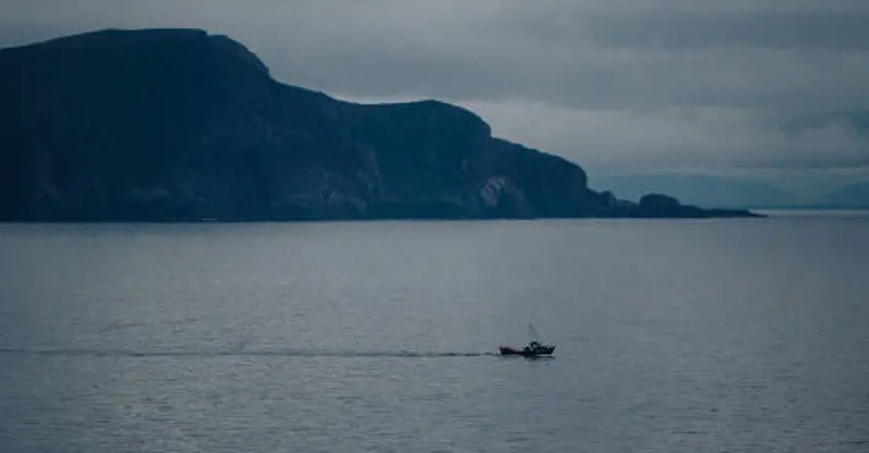Small fishing boat at sea with sea cliffs and headland in background